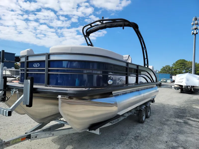 Slide: The Image of 2024 Harris Sunliner 230 Sport pontoon boat on a trailer under a blue sky. - 2