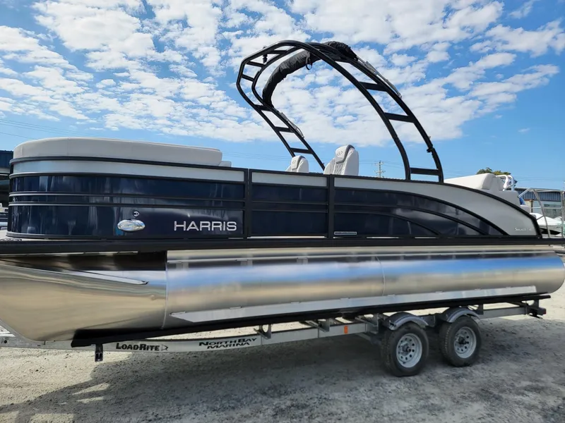 Slide: The Image of 2024 Harris Sunliner 230 Sport pontoon boat on a trailer under a blue sky. - 3