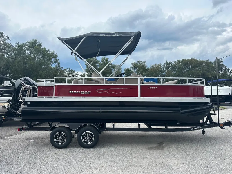 Slide: The Image of 2024 Ranger Reata 200F pontoon boat with black and red exterior, parked on a trailer. - 1