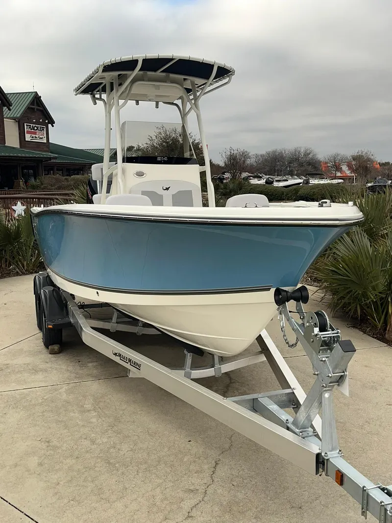 Slide: The Image of 2024 Mako 214 CC boat on trailer, blue hull, center console, T-top, outdoor display. - 2