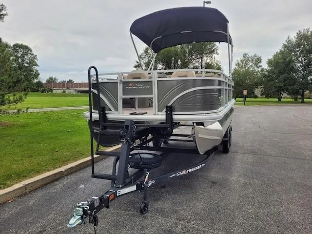 Slide: The Image of 2024 Sun Tracker Fishin' Barge 20 DLX pontoon boat on a trailer in a parking lot. - 2