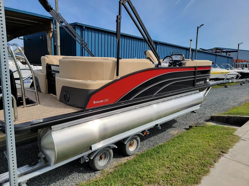 Slide: The Image of 2024 Harris Sunliner 210 pontoon boat on trailer, black and red exterior. - 2