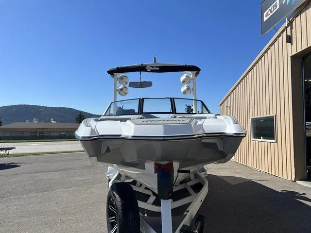 Slide: The Image of 2024 Malibu 23 MXZ boat on trailer, parked outside a building under clear blue sky. - 4