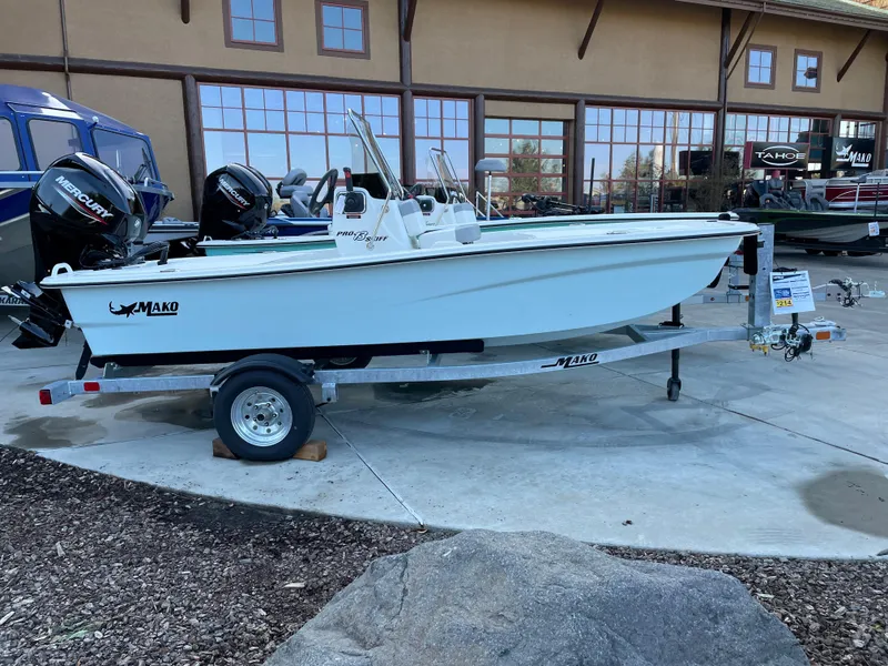 Slide: The Image of 2024 Mako Pro Skiff 13 CC boat on a trailer outside a showroom. - 1