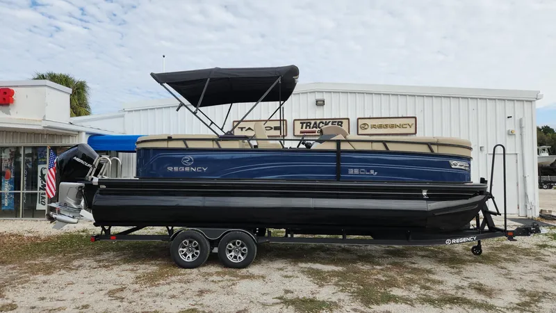 The Image of 2024 Regency 230 LE3 pontoon boat on trailer outside dealership. - 0