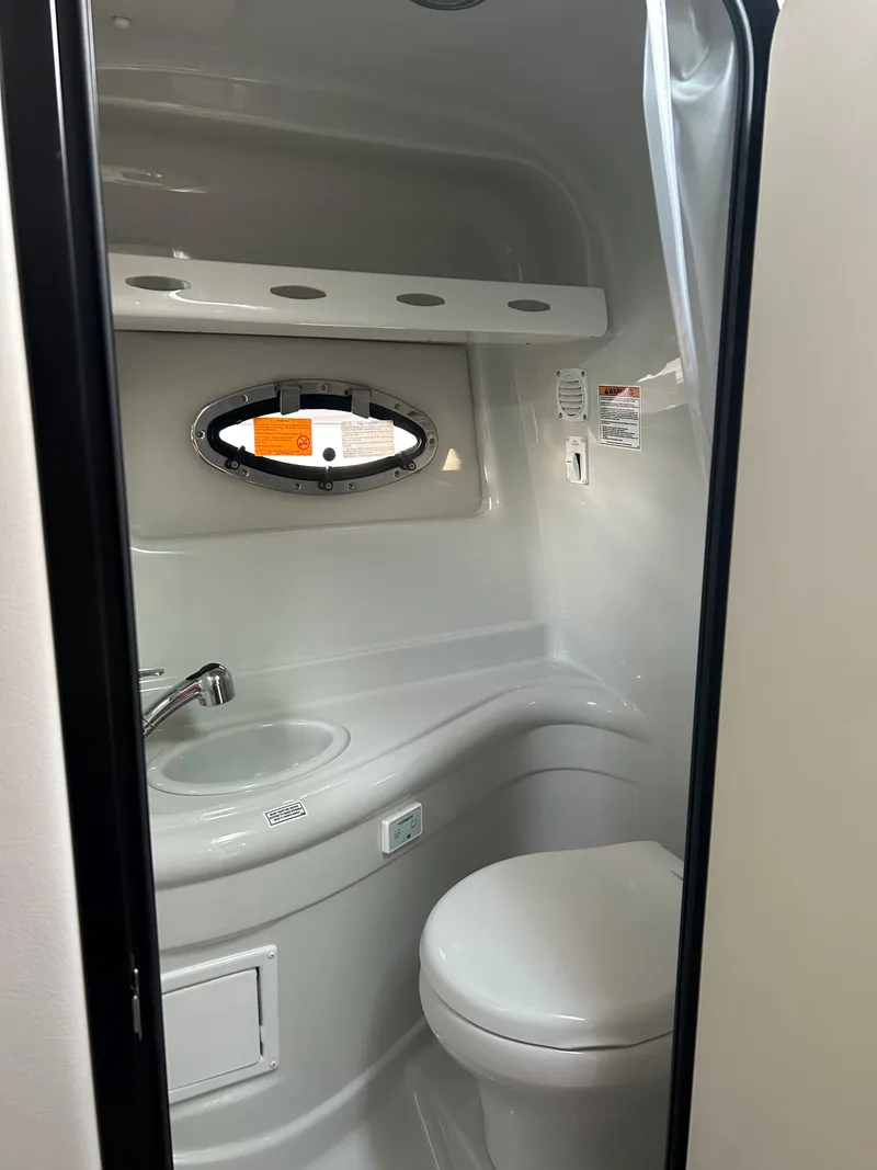 Slide: The Image of 2024 Crownline 270 CR boat bathroom with sink, toilet, and porthole window. - 17