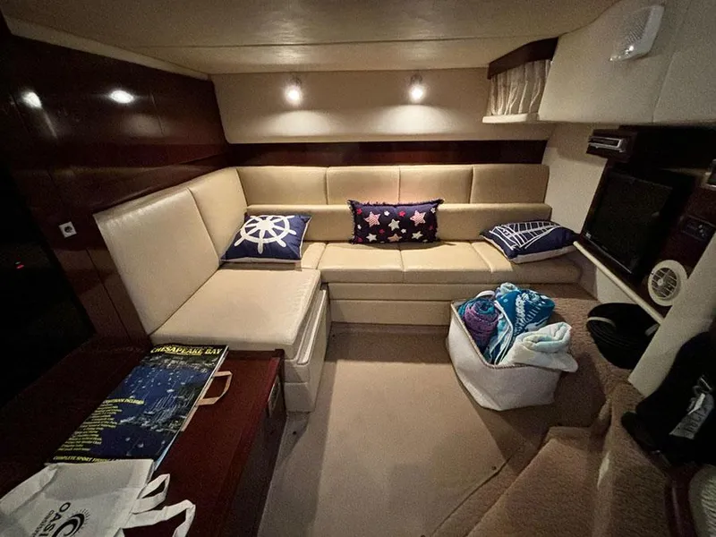 Slide: The Image of 2008 Sea Ray 38 Sundancer interior with beige seating, nautical-themed pillows, and cozy lighting. - 25