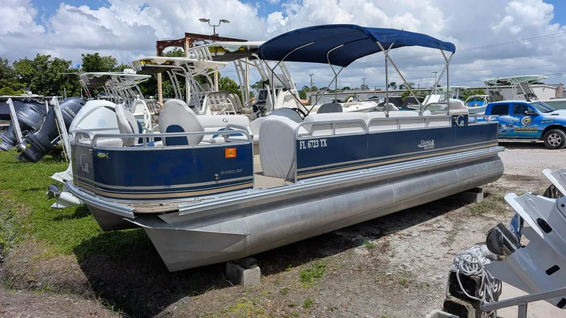The Image of 2016 Avalon 2480 QF pontoon boat with blue canopy, parked on grass. - 2