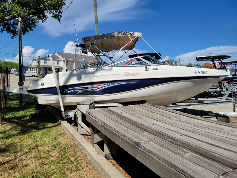 Slide: The Image of 2002 Rinker 212 BR boat on a wooden dock under a clear blue sky. - 2
