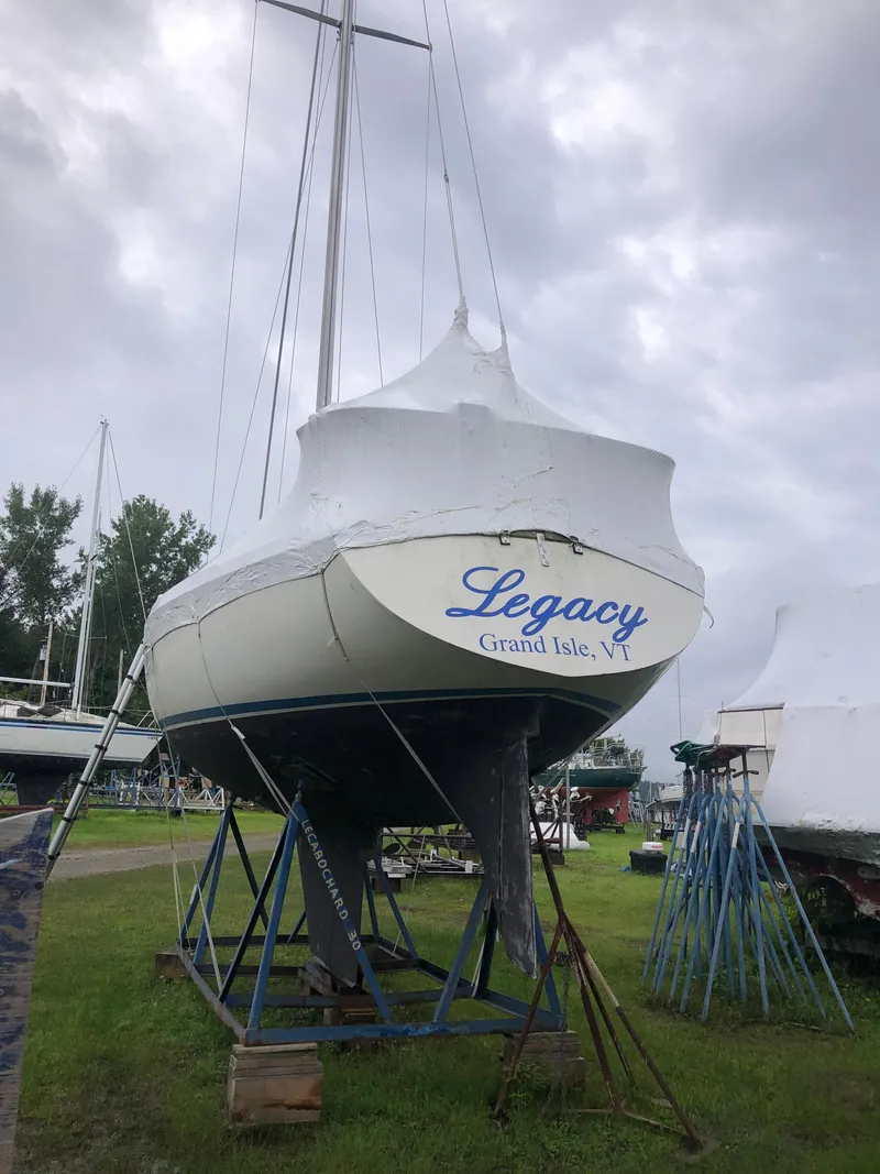 Slide: The Image of 1976 Tartan 30 sailboat named "Legacy" on stands, covered, under cloudy sky. - 7