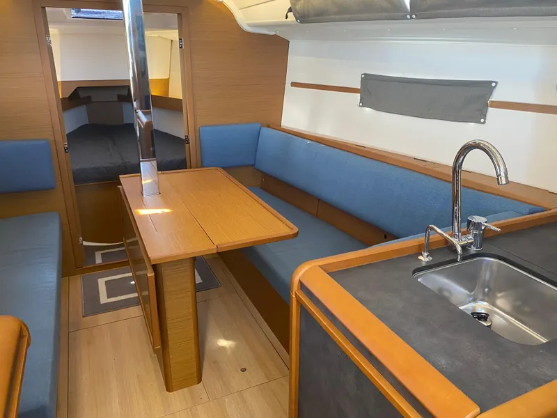 Slide: The Image of 2023 Jeanneau Sun Odyssey 349 interior with blue seating, wooden table, and compact kitchen area. - 18