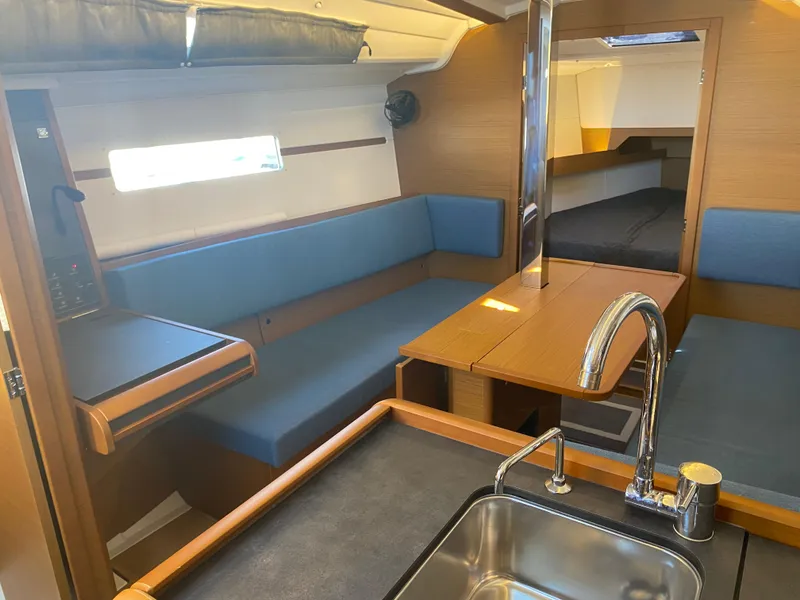 Slide: The Image of 2023 Jeanneau Sun Odyssey 349 interior with blue seating, wooden table, and modern kitchen sink. - 19