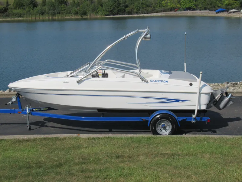 Slide: The Image of 2006 Glastron MX 195 boat on trailer by a lake, featuring sleek design and blue accents. - 0