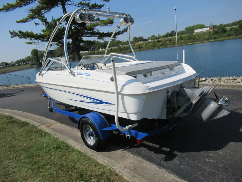 Slide: The Image of 2006 Glastron MX 195 boat on trailer by a lake, featuring sleek design and blue accents. - 1