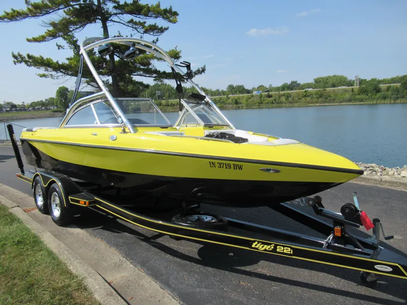 Slide: The Image of 2006 Tigé 22i yellow boat on trailer by a lake. - 8