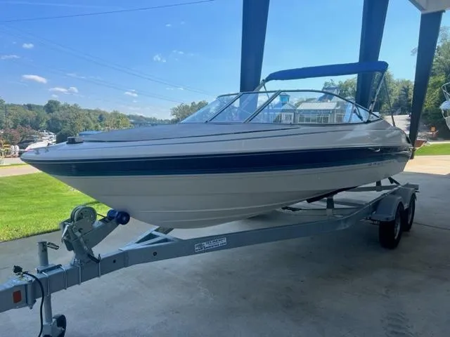 Slide: The Image of 1995 Bayliner 2050 Capri boat on trailer, parked outdoors under a canopy. - 2