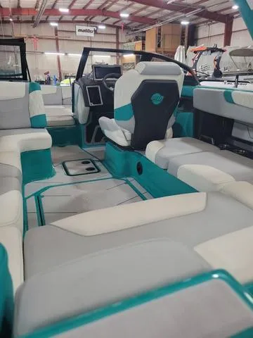 Slide: The Image of 2023 Malibu M220 boat interior with teal and white seating in a showroom. - 4
