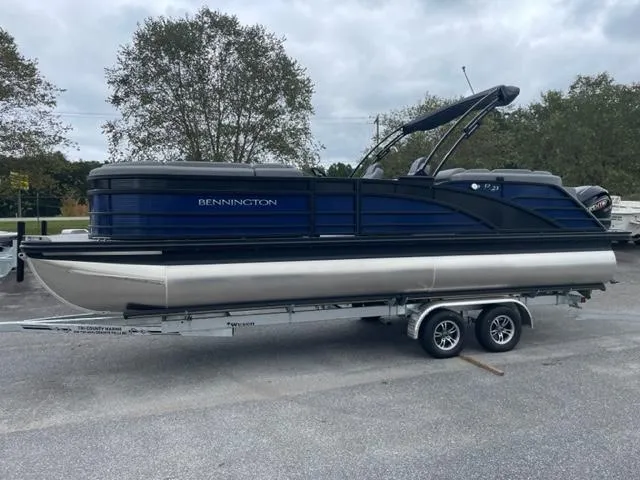 Slide: The Image of 2023 Bennington 23R pontoon boat on trailer, parked outdoors. - 2
