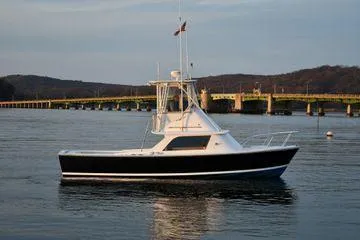 Slide: The Image of 1965 Bertram Sportfisher boat on calm water near a bridge, scenic background. - 5