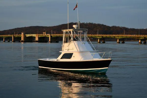 Slide: The Image of 1965 Bertram Sportfisher boat on calm water near a bridge at sunset. - 6