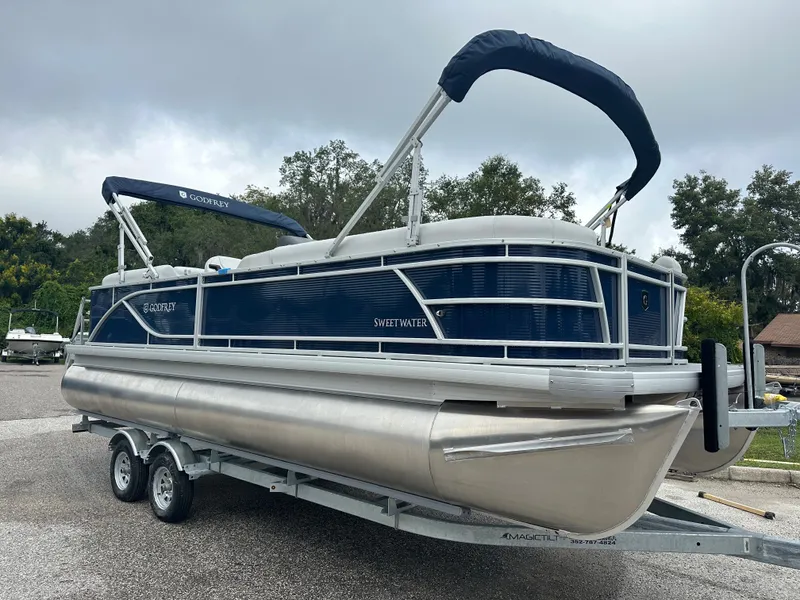 The Image of 2024 Sweetwater 2286 SB pontoon boat on trailer, blue and silver design. - 1