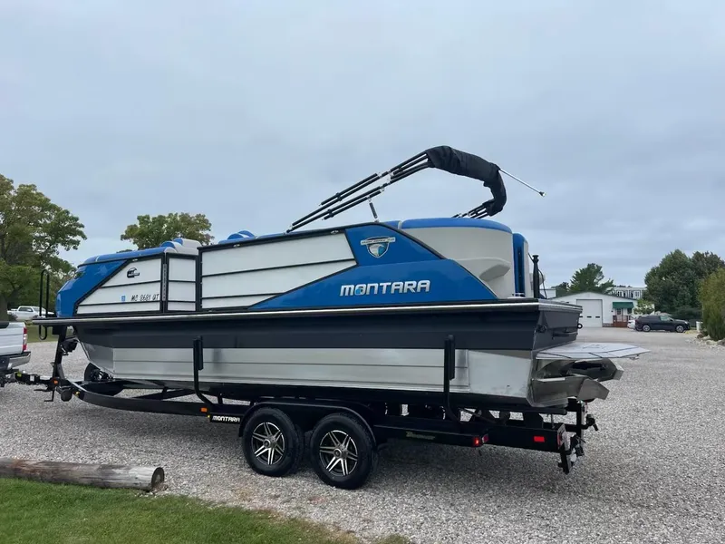The Image of 2021 Montara 23' Surfboss boat on trailer, blue and white design, parked outdoors. - 1