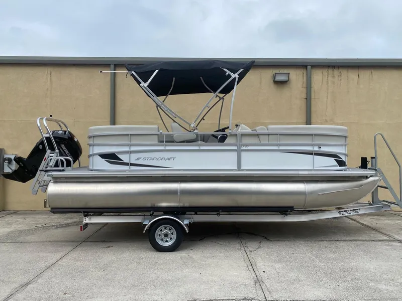 Slide: The Image of 2024 Starcraft LX 20 R pontoon boat on trailer, featuring a sleek design and canopy. - 1