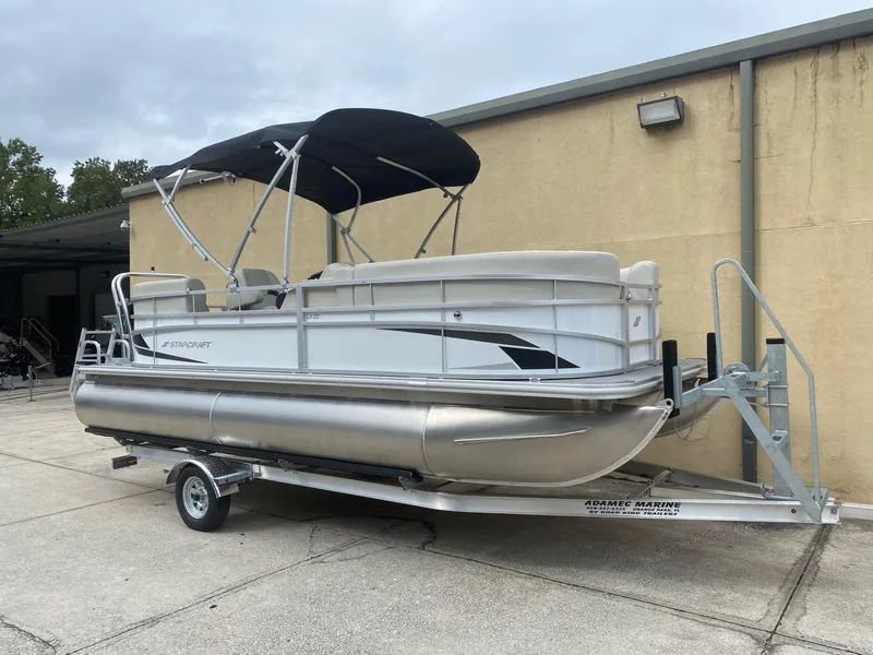 Slide: The Image of 2024 Starcraft LX 20 R pontoon boat on trailer, parked outdoors. - 2