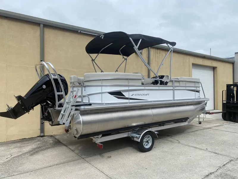 Slide: The Image of 2024 Starcraft LX 20 R pontoon boat on trailer, parked outdoors. - 3