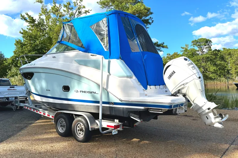 Slide: The Image of 2022 Regal 26XO boat with blue canopy on trailer, parked outdoors. - 49