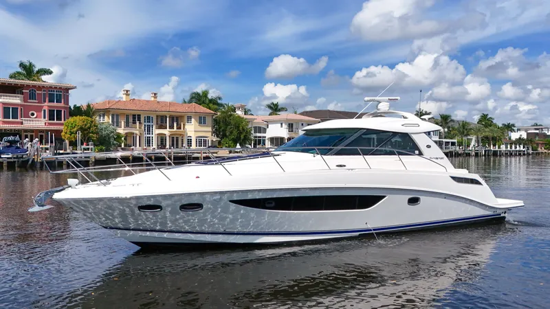 The Image of 2013 Sea Ray 450 Sundancer yacht cruising near waterfront homes under a blue sky. - 0