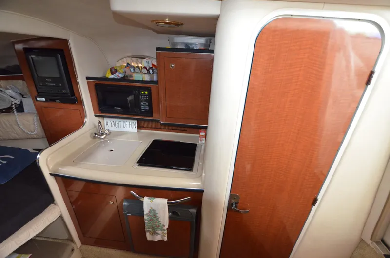 Slide: The Image of 2003 Sea Ray 280 DA galley with sink, stove, microwave, and wooden cabinetry. - 16