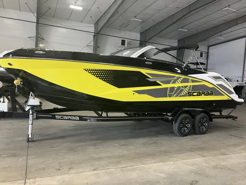 Slide: The Image of 2024 Scarab 285 boat in yellow and black, displayed indoors on a trailer. - 2