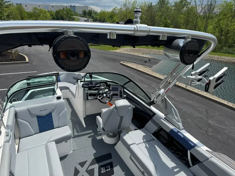 Slide: The Image of 2023 MasterCraft XT23 boat interior with sleek seating and advanced controls, docked near a scenic pond. - 14