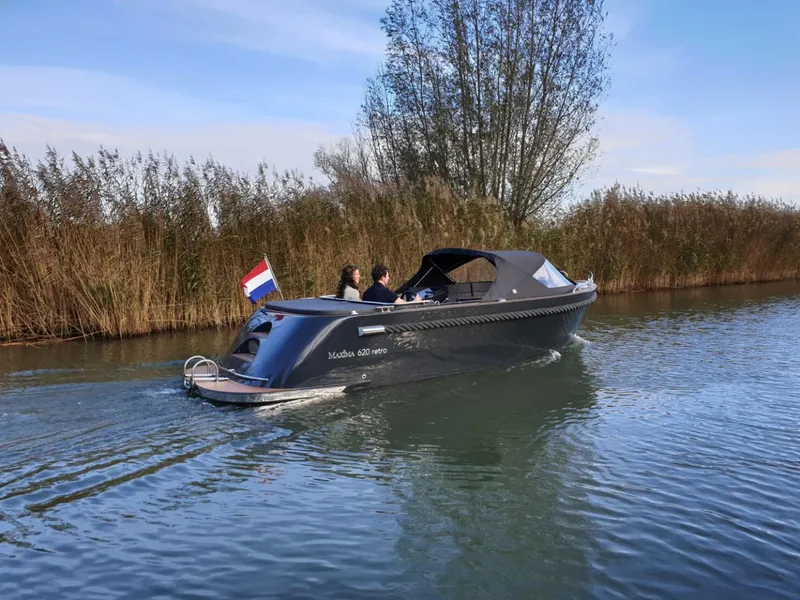 Slide: The Image of 2023 Maxima 620 Retro boat cruising on a calm river with reeds in the background. - 15