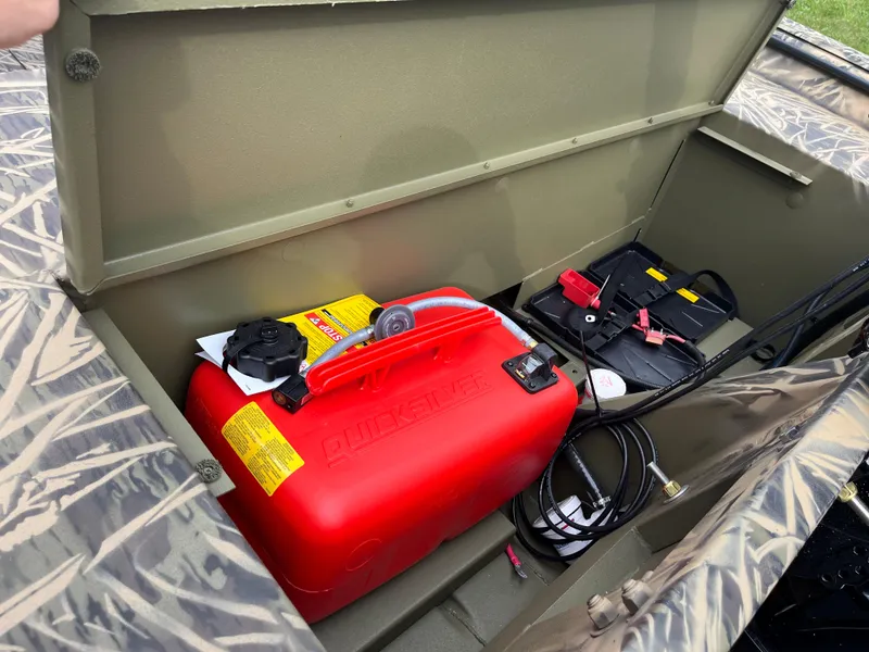 Slide: The Image of 2024 Lowe Roughneck 1660 storage compartment with red fuel tank and battery. - 14