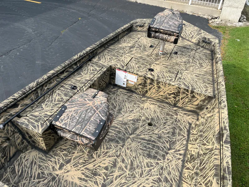 Slide: The Image of 2024 Lowe Roughneck 1660 camo boat interior with seating and storage compartments. - 6