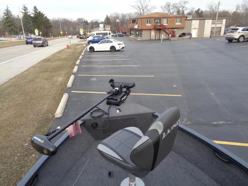 Slide: The Image of 2024 Lund 1650 Rebel XL Sport boat parked in a lot, featuring a swivel seat and trolling motor. - 24