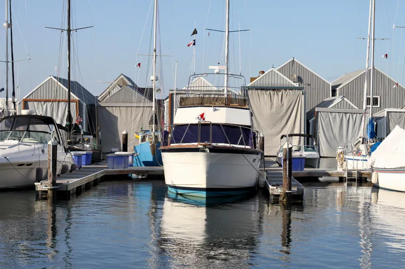 Slide: The Image of 1977 Hatteras 37 Convertible docked at a marina with boat houses in the background. - 43