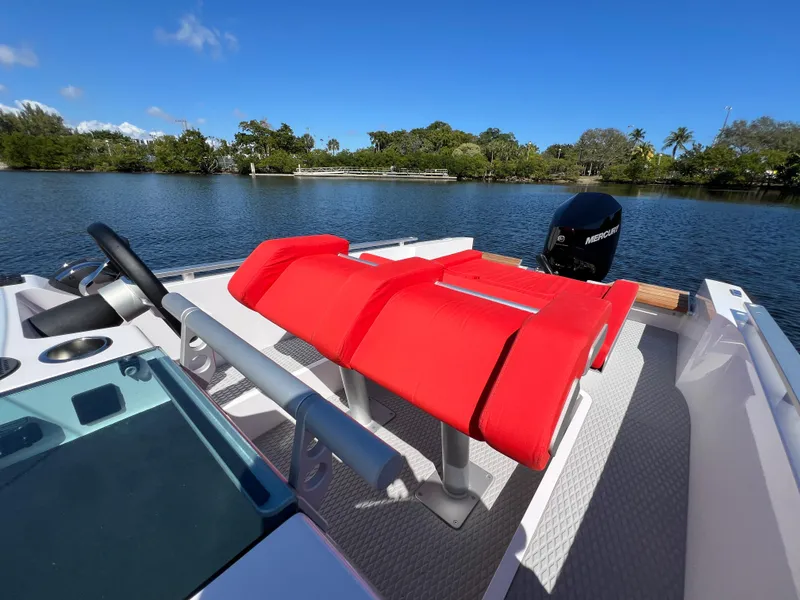 Slide: The Image of 2021 Goldfish 23 Tender boat with red seating, steering wheel, and outboard motor on a calm lake. - 25