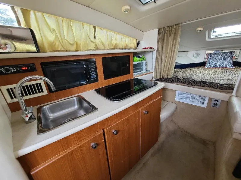 Slide: The Image of 2003 Bayliner 285 Ciera interior with kitchenette, sink, microwave, and cozy sleeping area. - 8