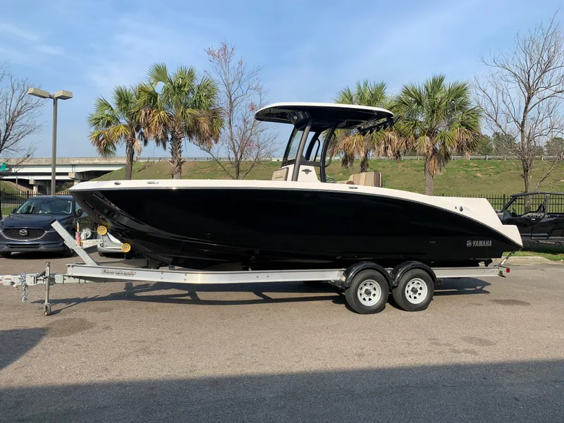 The Image of 2023 Yamaha Boats 255 FSH Sport E on trailer, black hull, palm trees in background. - 1
