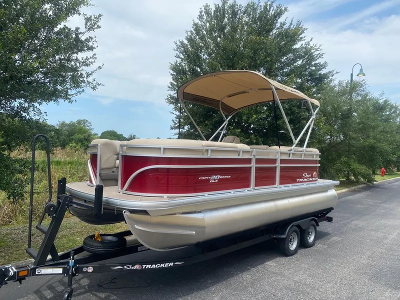 The Image of 2024 Sun Tracker Party Barge 20 DLX pontoon boat on trailer, red and beige color scheme. - 0