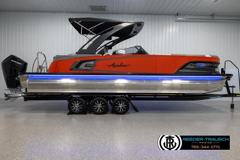 Slide: The Image of 2024 Avalon 2785 Excalibur EL pontoon boat with orange and black design on trailer. - 11