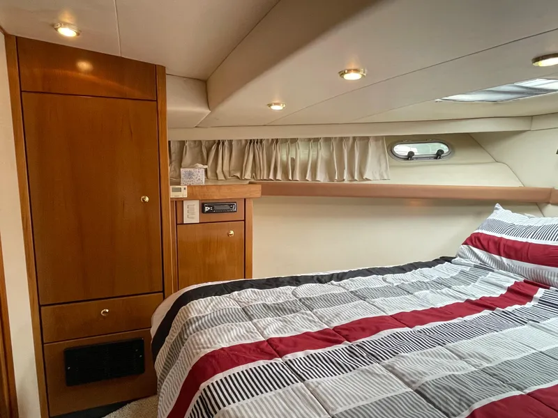 Slide: The Image of 1998 Bayliner 4788 Pilot House Motoryacht bedroom with striped bedding and wooden cabinetry. - 33
