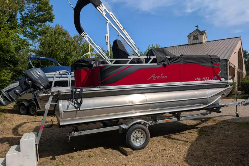 Slide: The Image of 2023 Avalon VENTURE CRUISE pontoon boat on trailer, red and silver design, parked outdoors. - 1