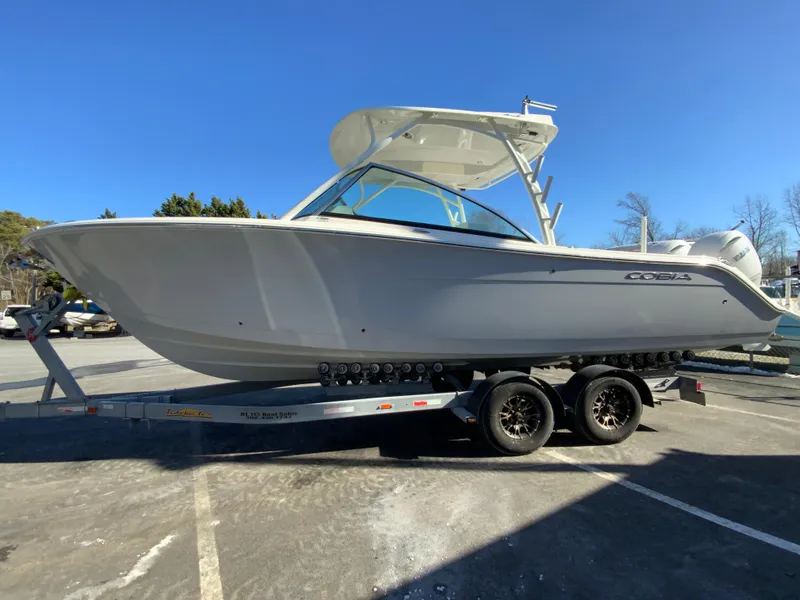 Slide: The Image of 2025 Cobia 280 Dual Console boat on trailer, parked outdoors under clear blue sky. - 7