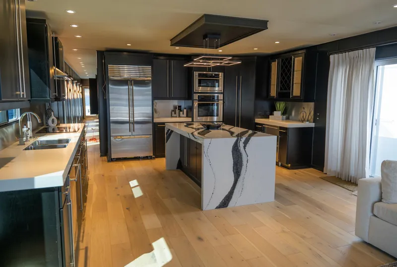 Slide: The Image of Modern kitchen with black cabinets, marble island, stainless steel appliances, and light wood flooring. - 22
