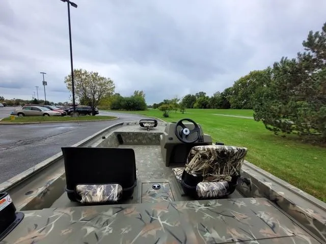 Slide: The Image of 2024 Tracker Grizzly 1754 SC boat with camo seats and steering wheel, parked outdoors. - 5