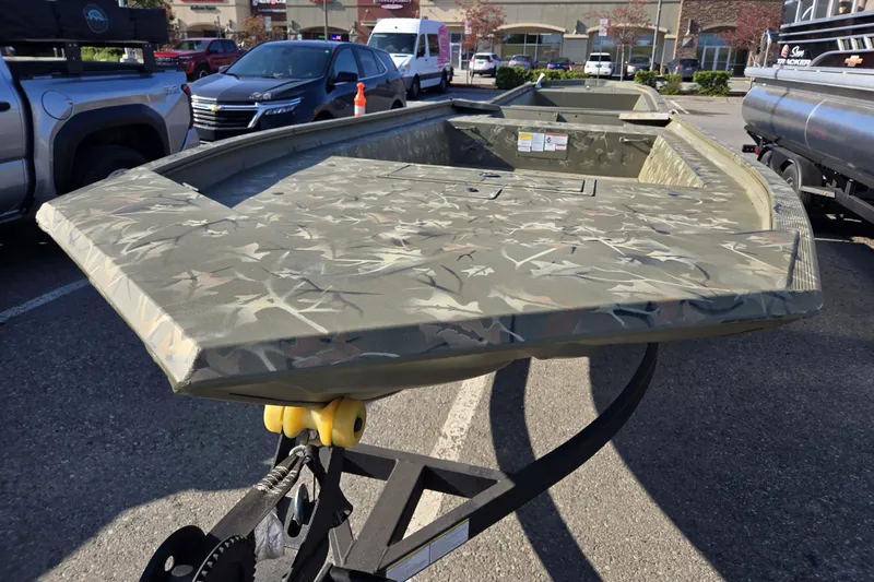 Slide: The Image of 2024 Tracker Grizzly 1754 Jon boat with camouflage design on a trailer in a parking lot. - 2